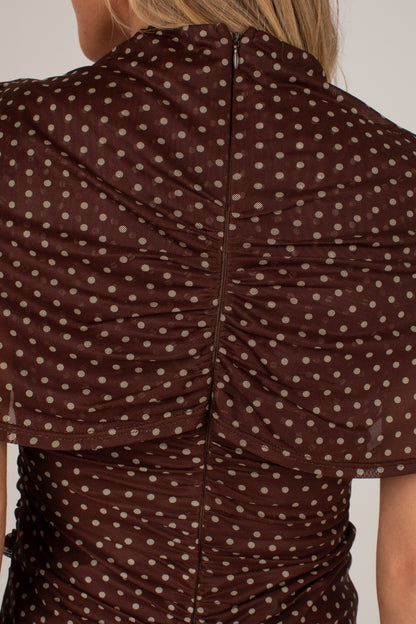 Close-up back view of a woman wearing a brown sheer mesh top with beige polka dots and ruched detailing.