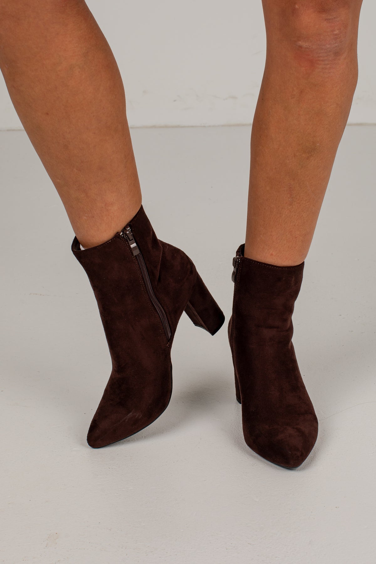 A pair of dark brown suede ankle boots with pointed toes and block heels, shown on a model&