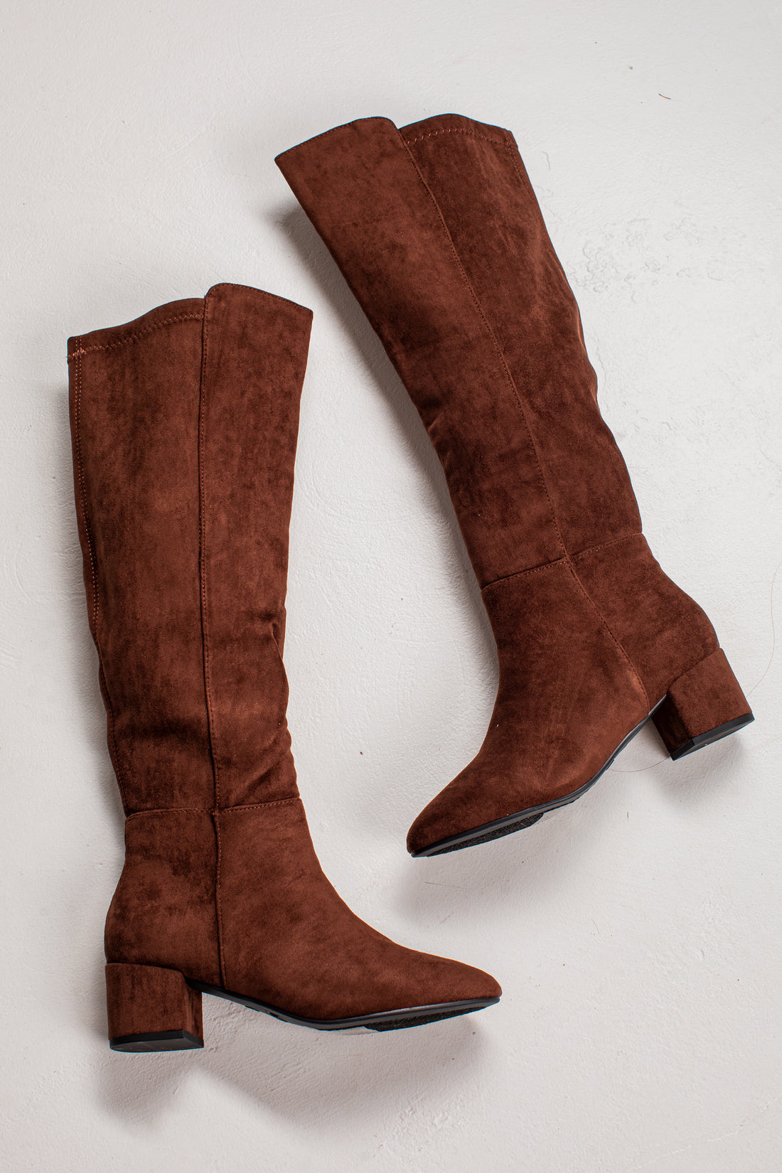 A pair of knee-high brown suede boots with block heels, shown from different angles on a light off-white background.