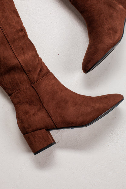 A pair of brown suede over-the-knee boots with a low block heel and pointed toe, shown on a textured off-white background.