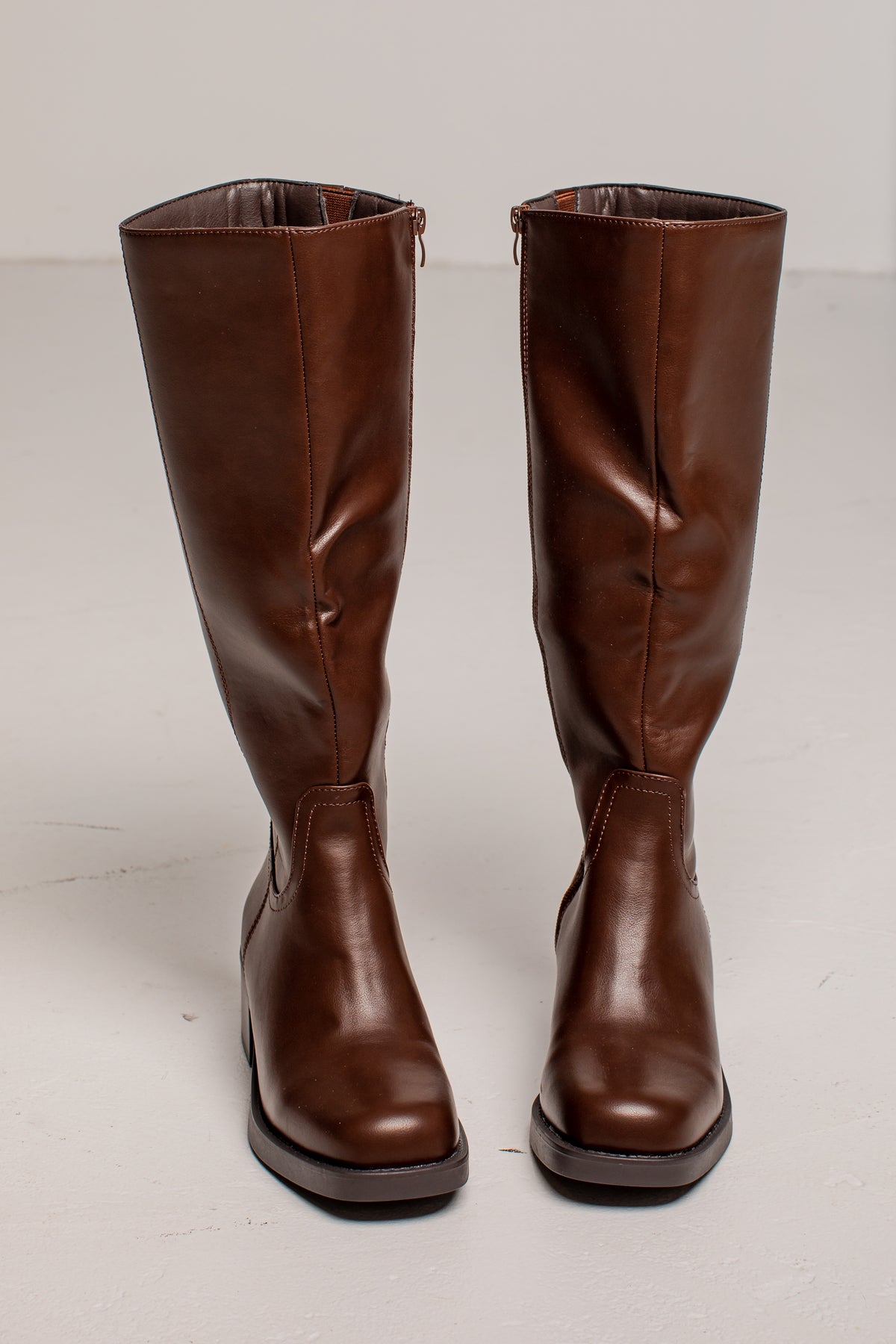 A pair of knee-high brown leather boots with a slight sheen, shown from the front against a plain light gray background.