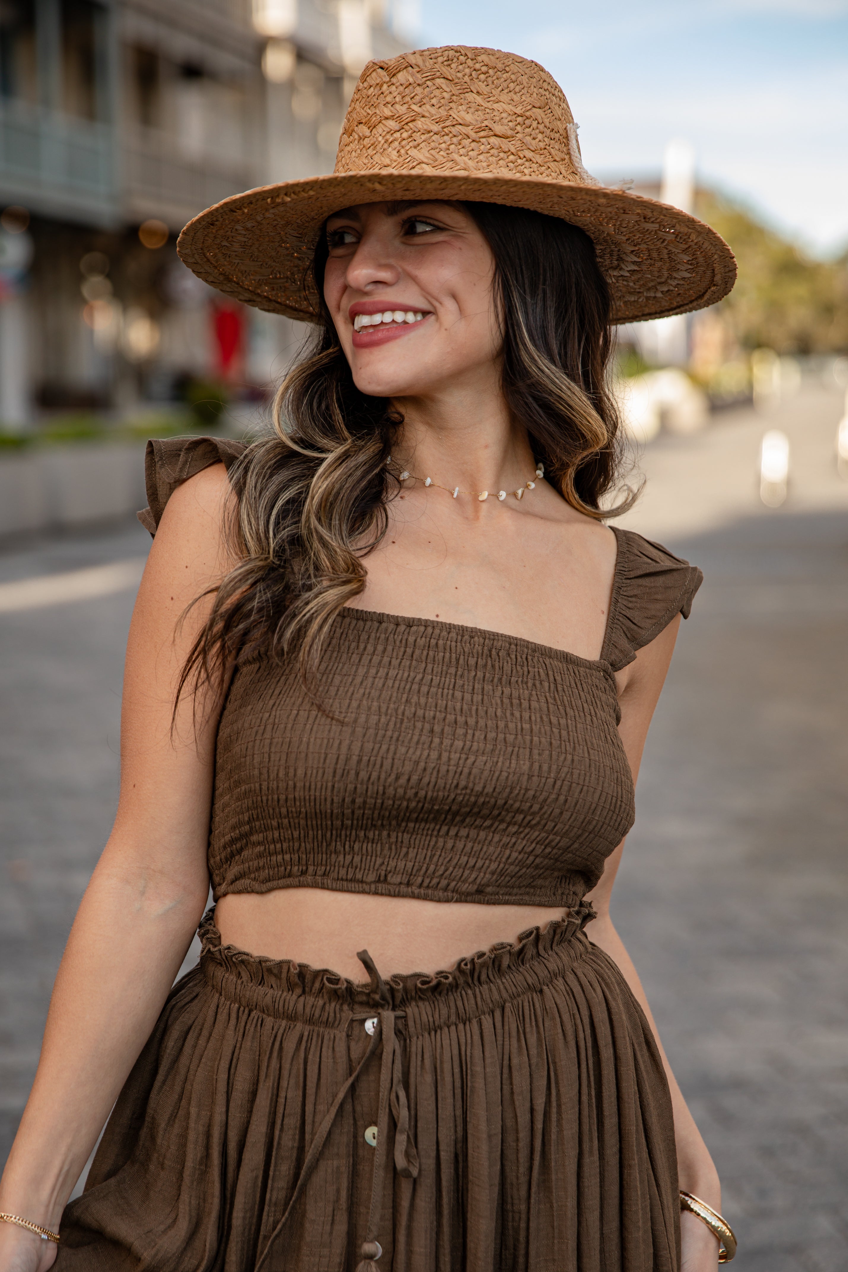 Woman wearing a brown outfit with a straw hat on a street.
