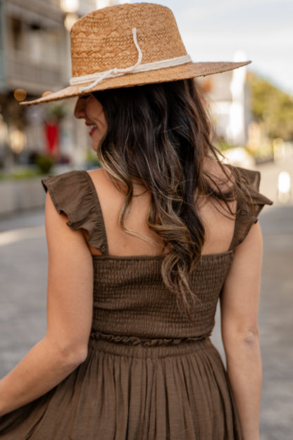Woman wearing a brown dress and straw hat in an outdoor setting