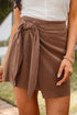 Person wearing a brown wrap skirt with a white top outdoors.