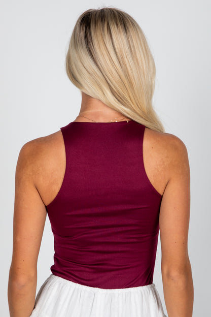 Person wearing a burgundy sleeveless top with a plain background