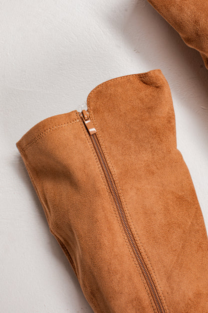 Close-up of a tan suede or faux-suede garment with a visible center zipper, laid on a light neutral background.