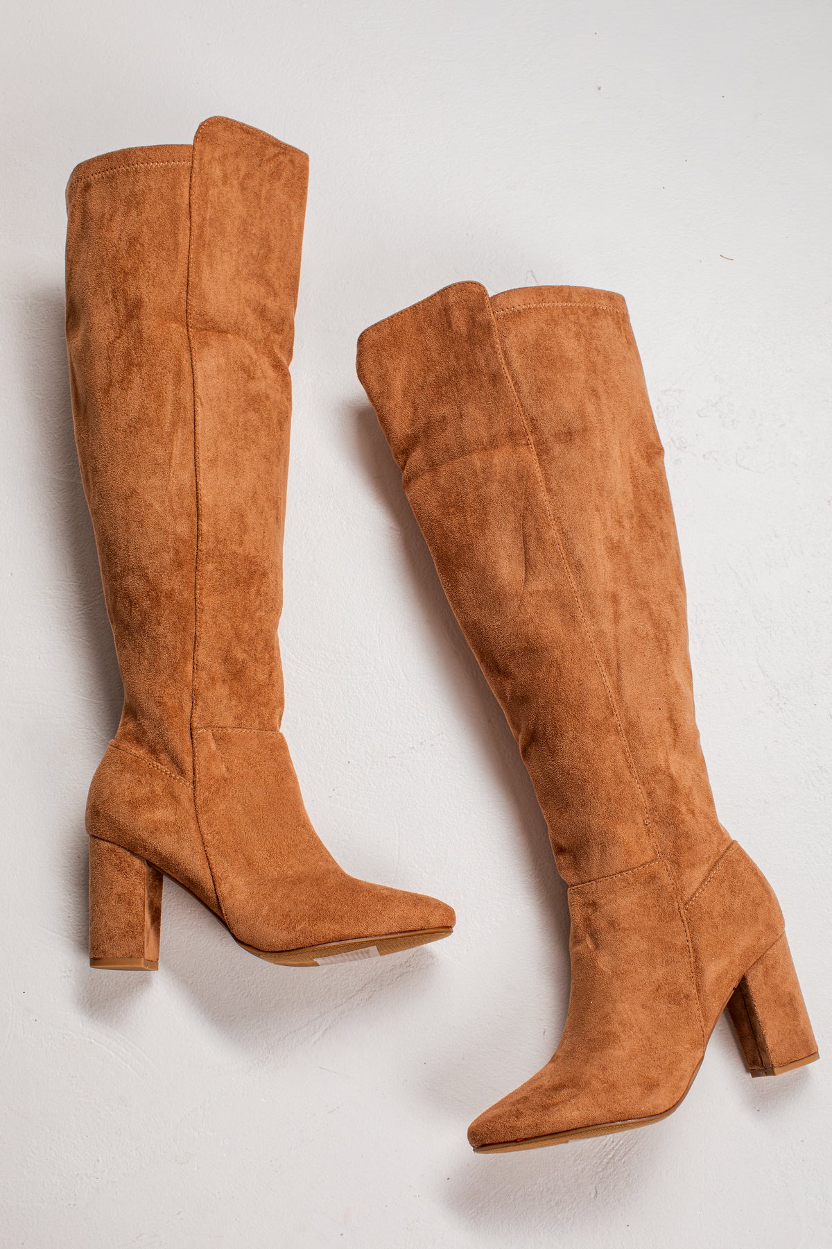 A pair of knee-high suede boots in a warm camel brown color, featuring a block heel and pointed toe, displayed on a light off-white background.