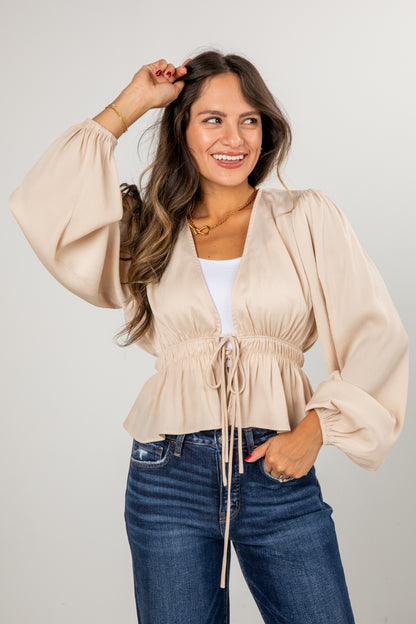 Woman wearing a beige top and blue jeans against a plain background