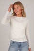A woman wearing a cream-colored, textured long-sleeve knit sweater and light blue jeans, posing against a solid light gray background.