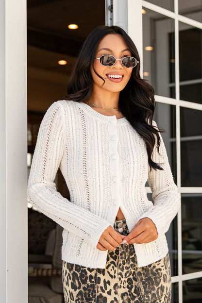 Woman wearing a white sweater and leopard print pants standing in front of a glass door.