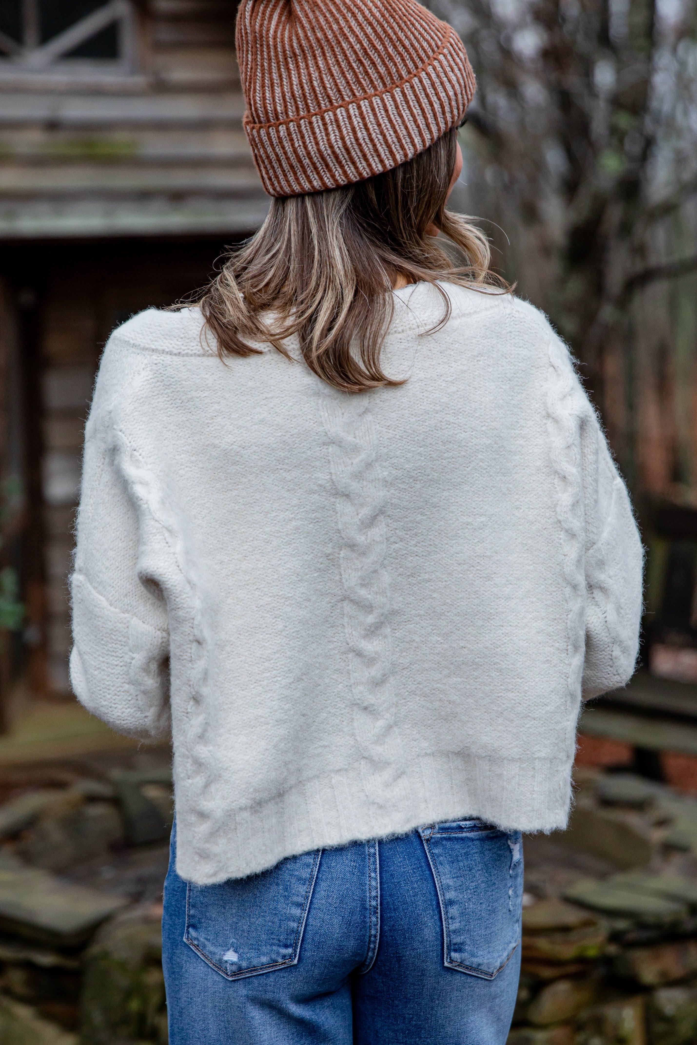 Person wearing a white fluffy jacket and brown beanie with back turned, standing outdoors.