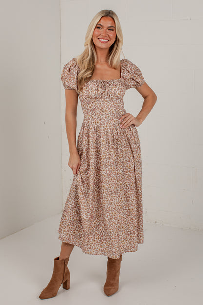 A woman modeling a midi-length puff-sleeve dress with a small-scale floral print in beige, brown, and muted orange tones, paired with brown ankle boots, set against a plain white studio background.