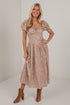 A woman modeling a midi-length puff-sleeve dress with a small-scale floral print in beige, brown, and muted orange tones, paired with brown ankle boots, set against a plain white studio background.