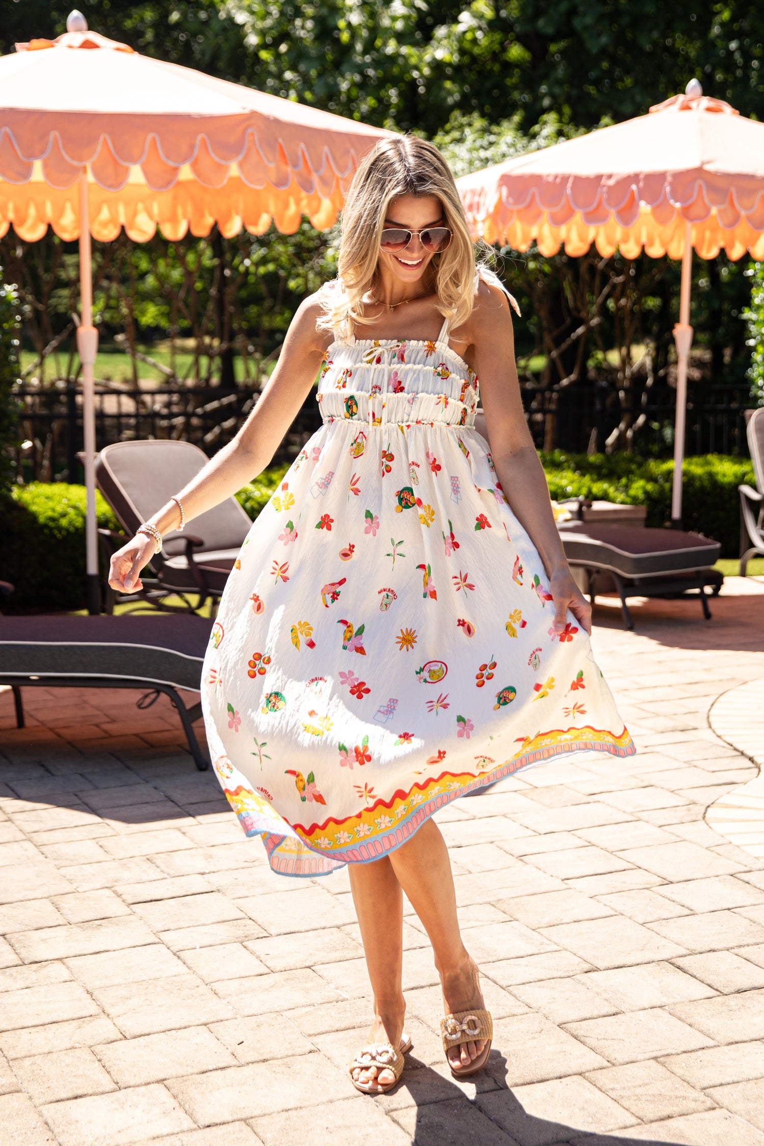 Woman in a floral dress standing outdoors with patio furniture and umbrellas in the background