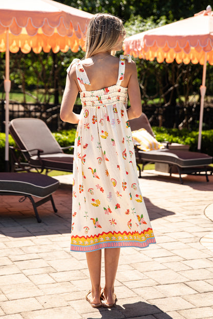 Woman in a floral dress standing on a patio with outdoor furniture and umbrellas.