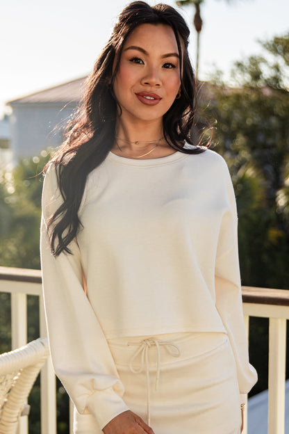 Woman wearing a white outfit on a balcony with greenery in the background