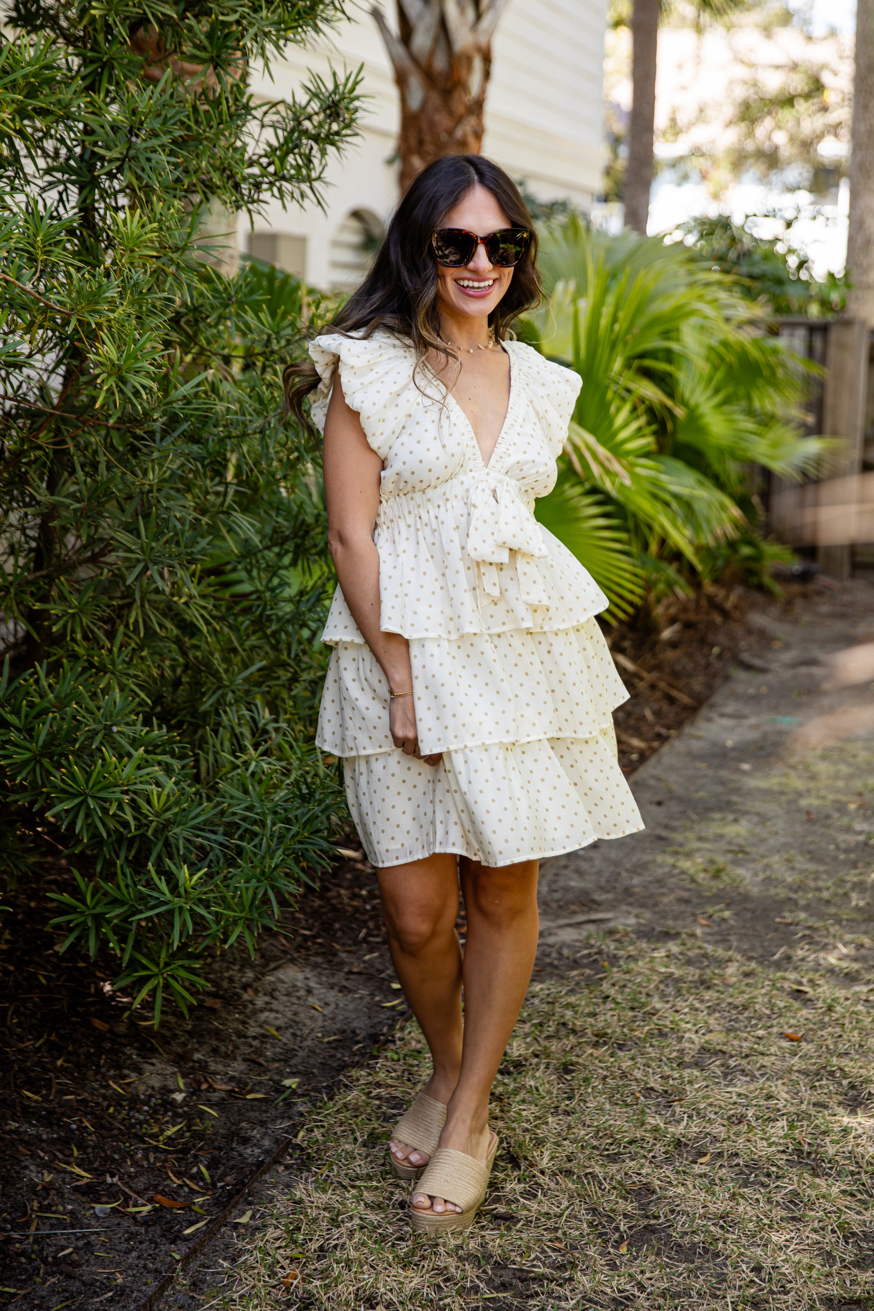 Woman in a white floral dress standing outdoors with greenery around