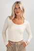 Woman wearing a beige long-sleeve top and beige pants against a plain background