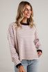 A woman wearing a long-sleeve knit top with thin horizontal stripes in beige and purple, featuring dark navy ribbed trim at the crew neck, cuffs, and hem, paired with light-wash blue jeans.