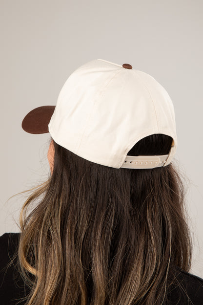 Person wearing a white cap with a brown brim on a plain background