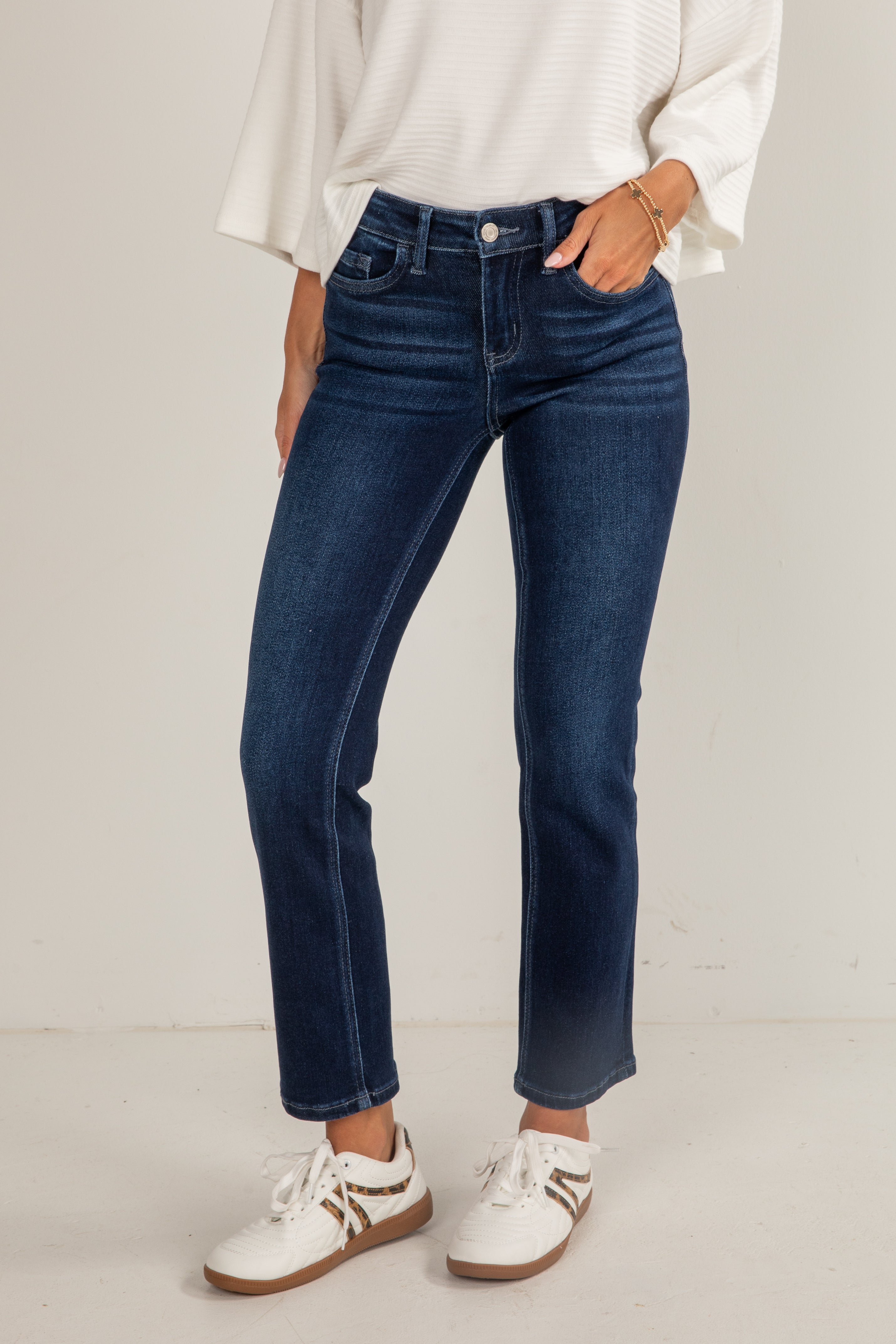 Person wearing blue jeans and white sneakers on a plain background