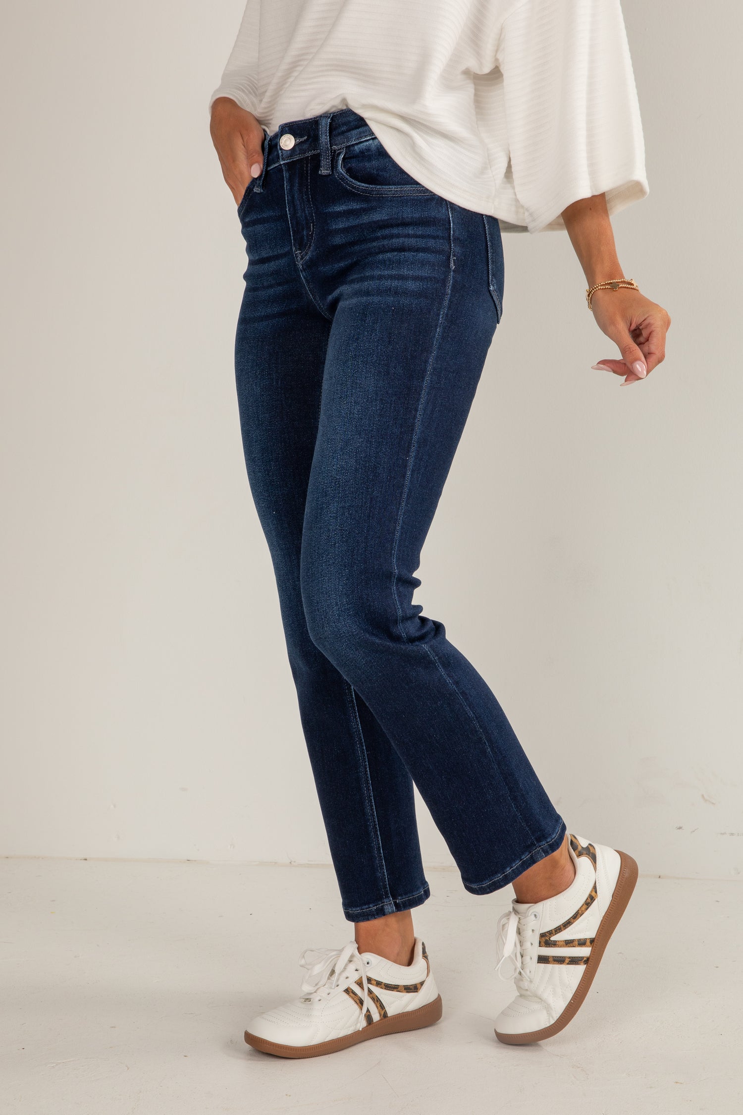 Person wearing blue jeans and white sneakers on a plain background