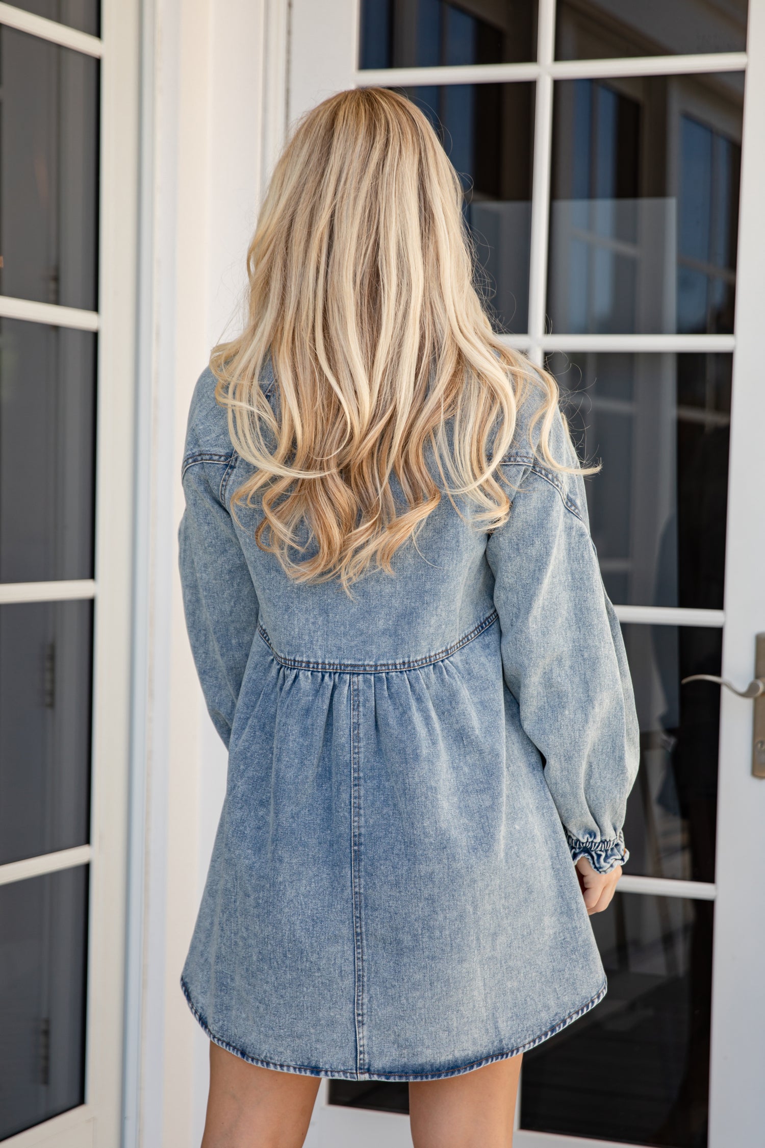 Person wearing a denim dress standing in front of a glass door.