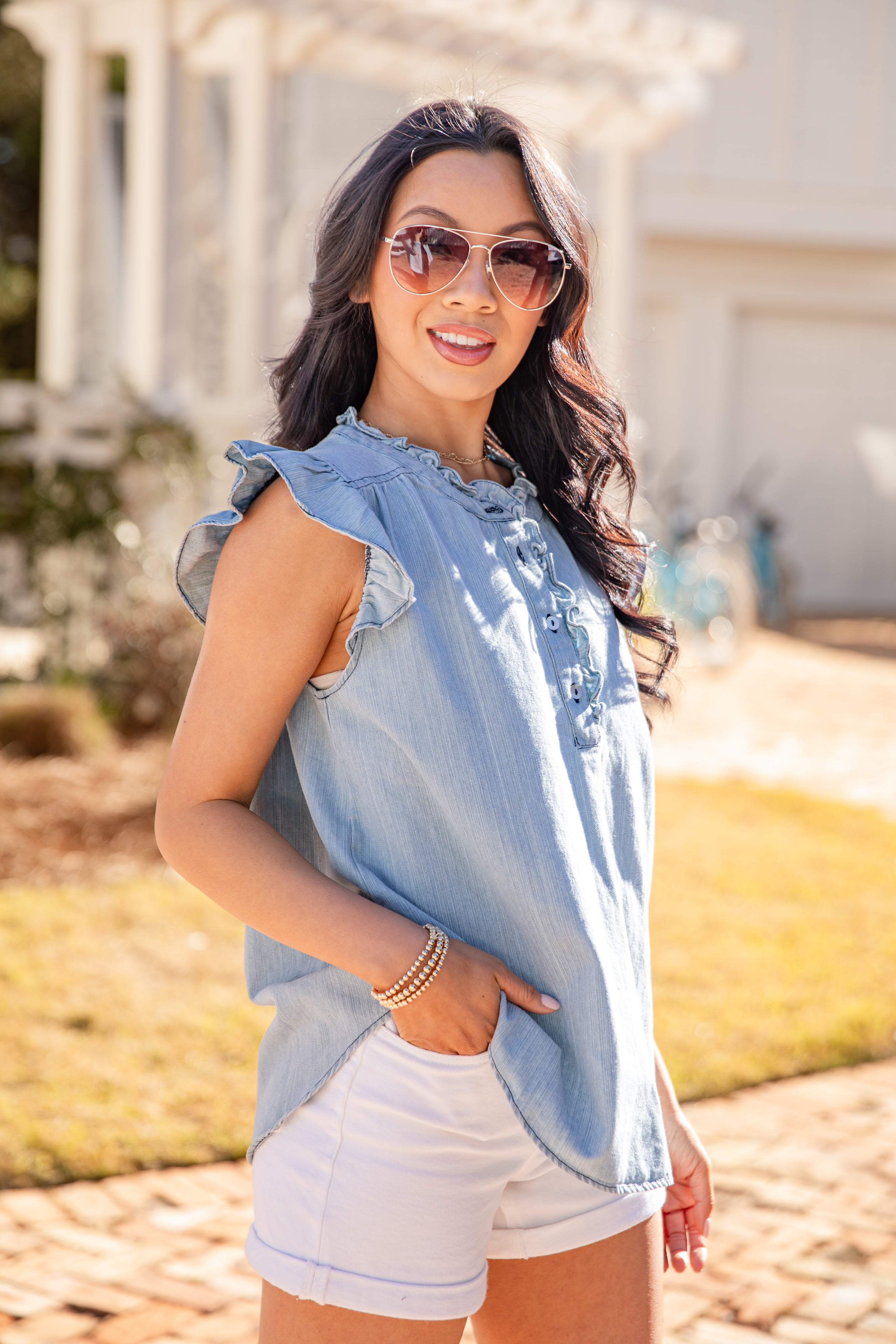 Woman wearing a light blue denim top and white shorts outdoors.