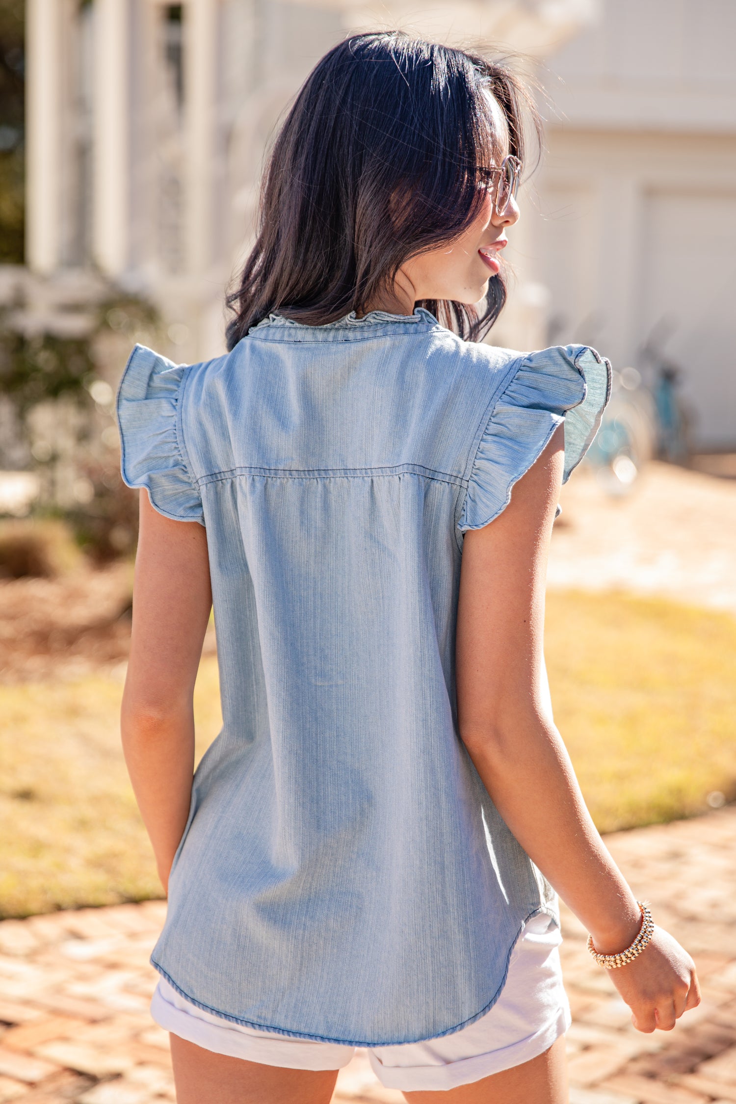 Woman wearing a light blue denim shirt with ruffled sleeves outdoors.