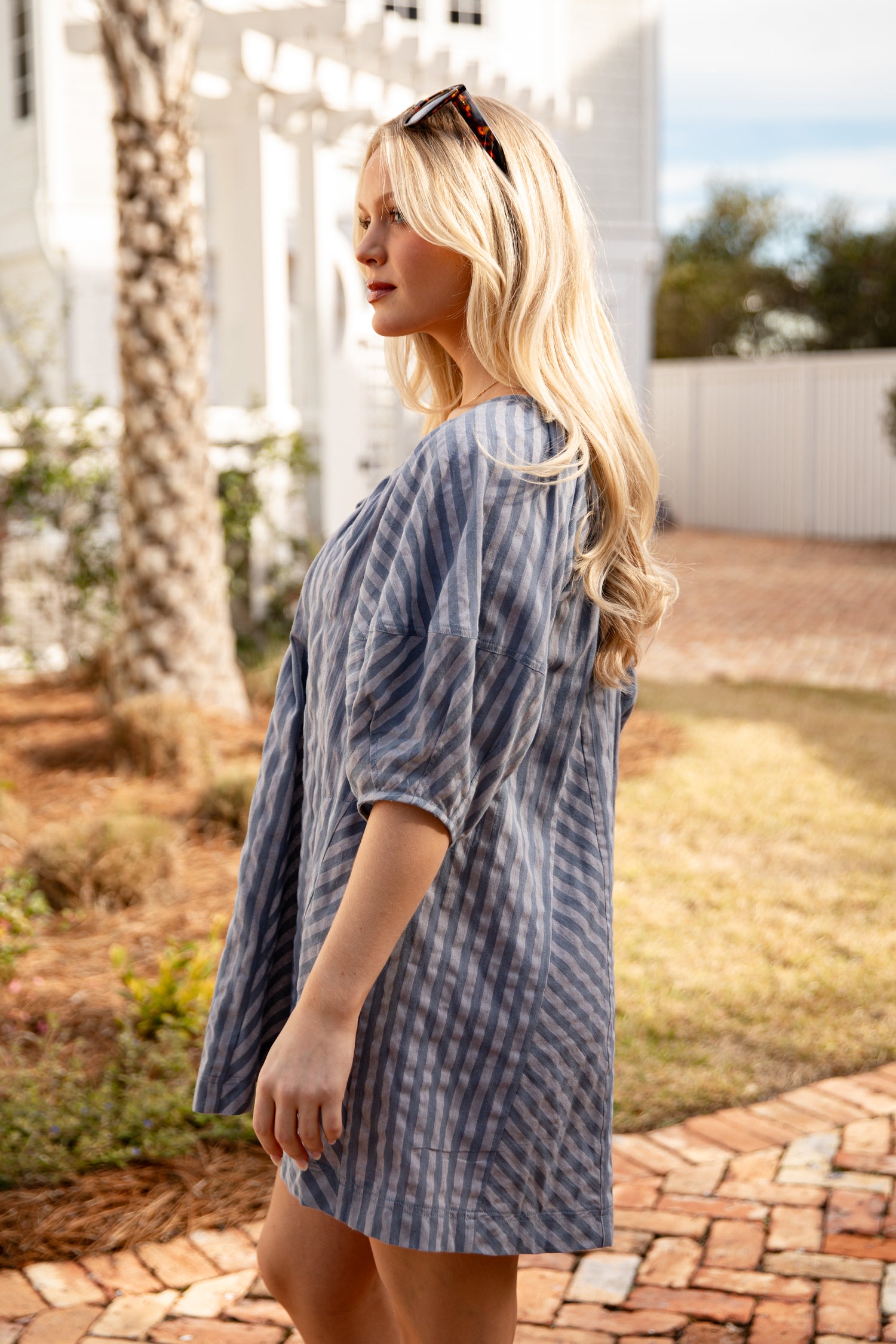 Woman wearing a blue patterned dress standing outdoors on a sunny day.