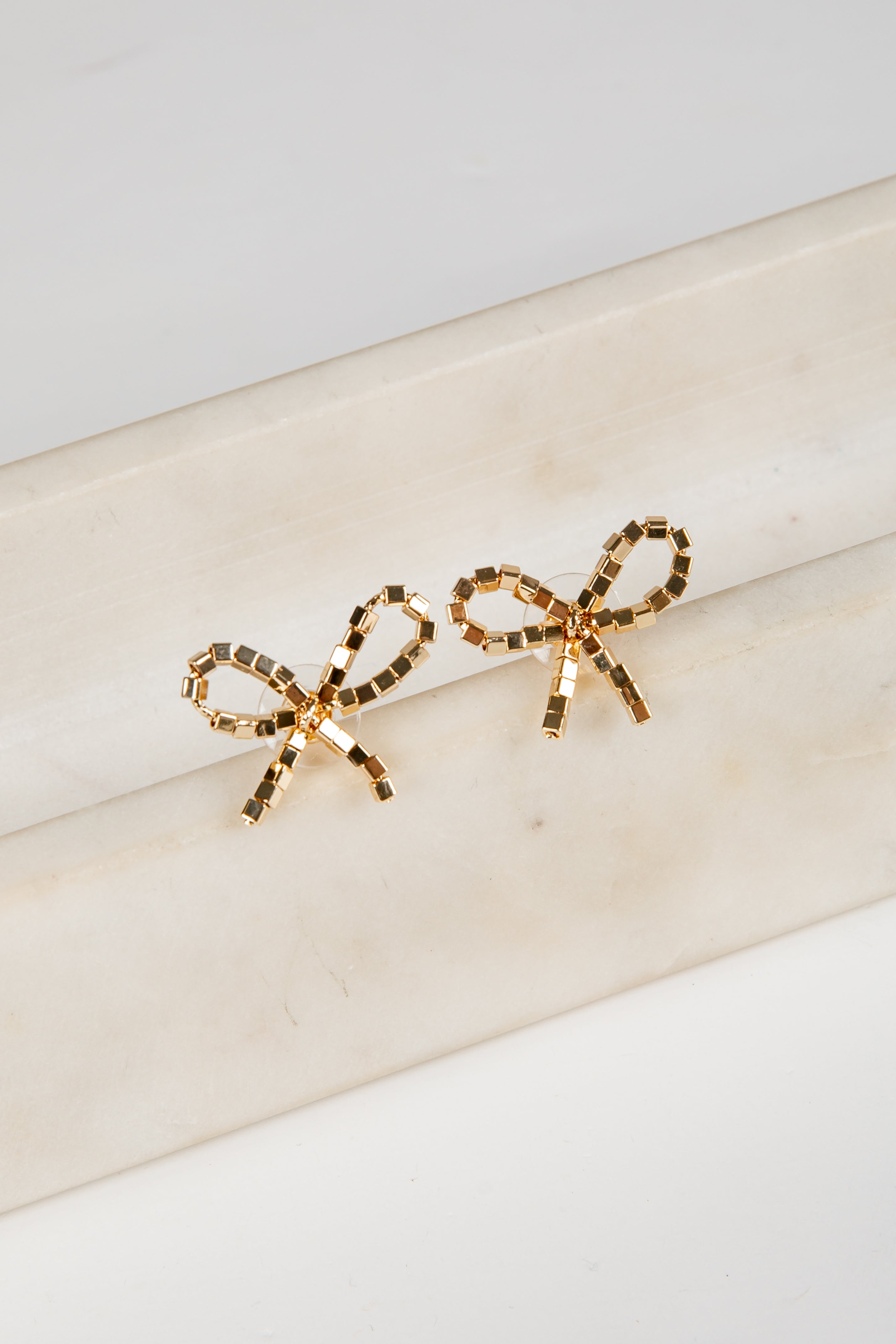 Gold bow-shaped earrings on a marble surface