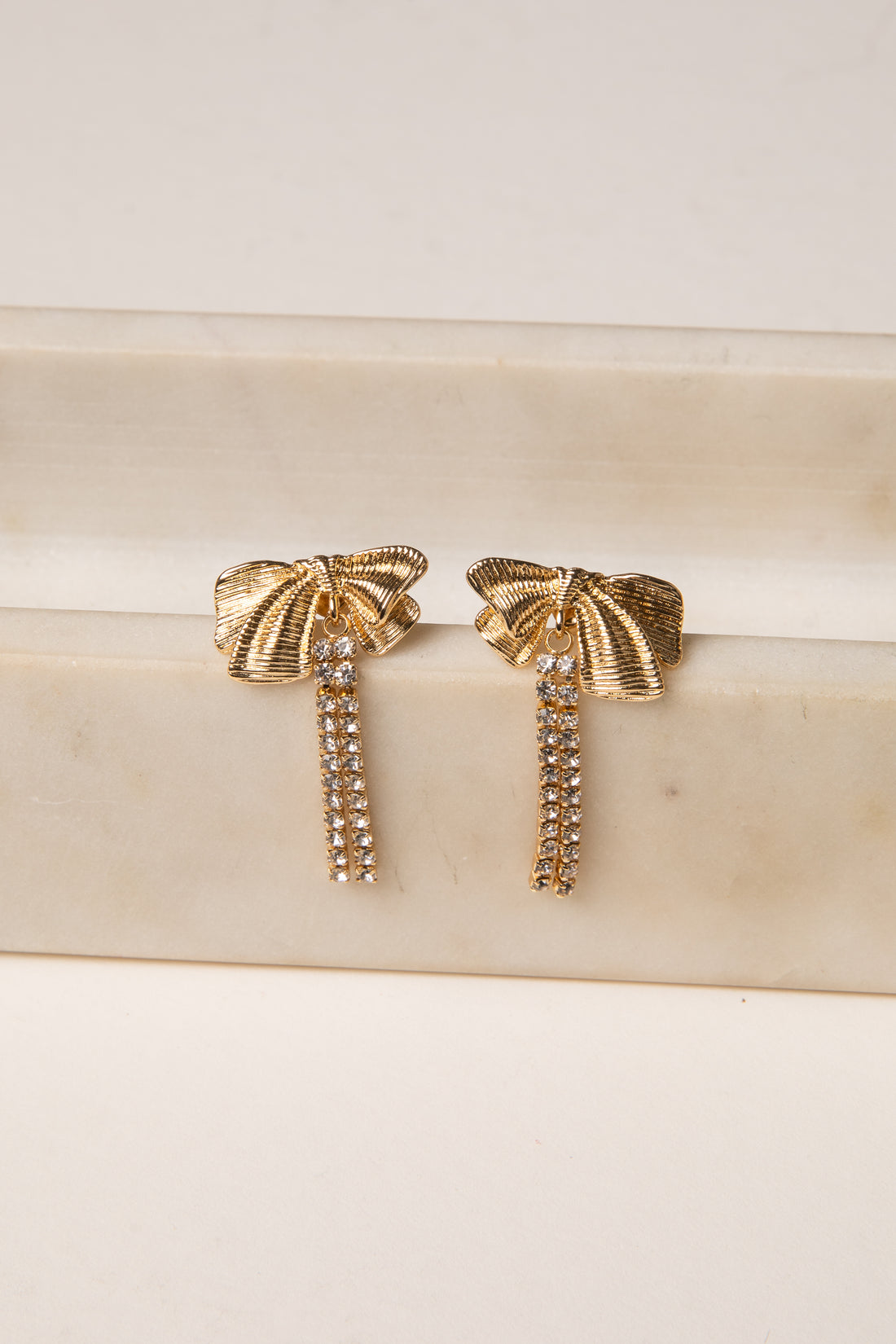 Gold bow-shaped earrings on a marble surface