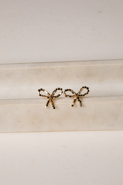 Gold bow-shaped earrings on a marble surface