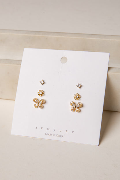 Gold floral earrings on a white jewelry card with a beige background