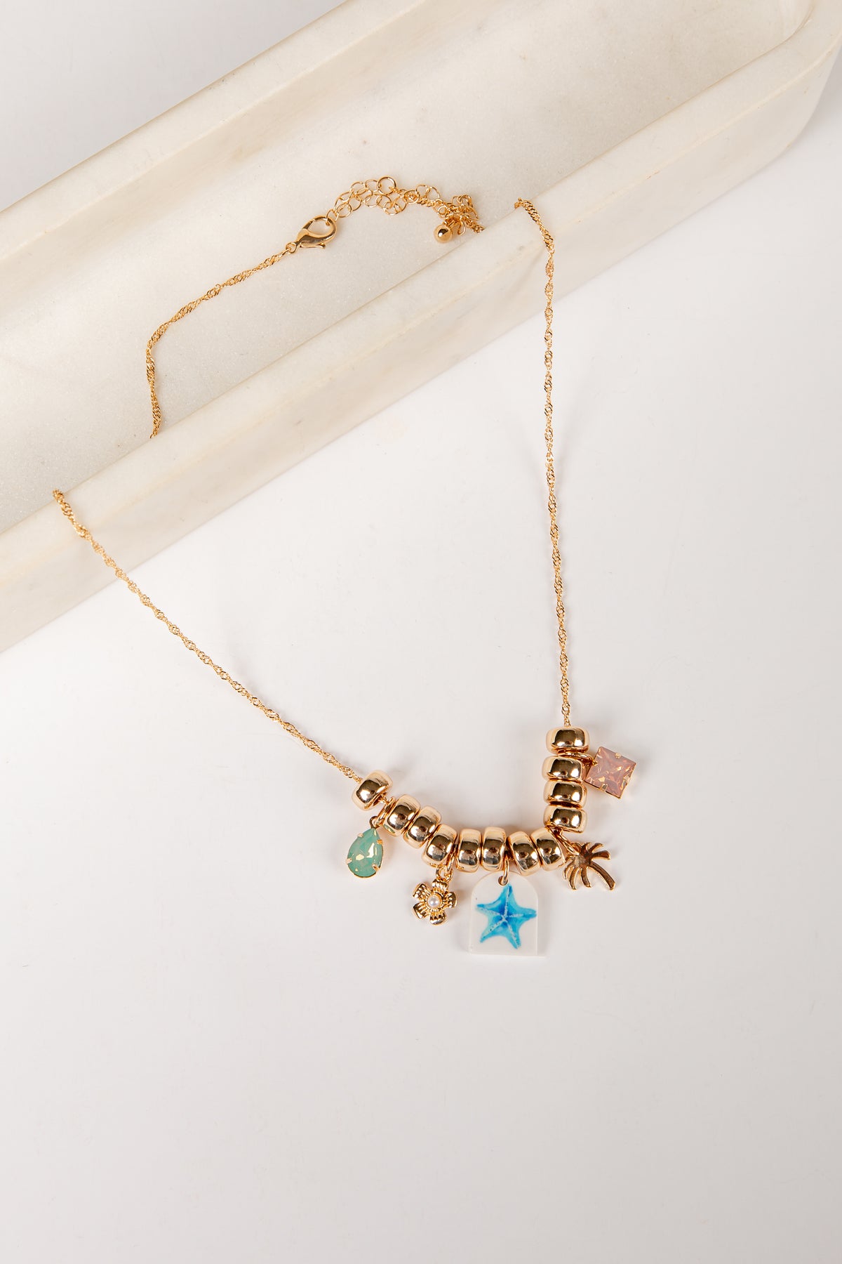 Gold necklace with various charms on a white background