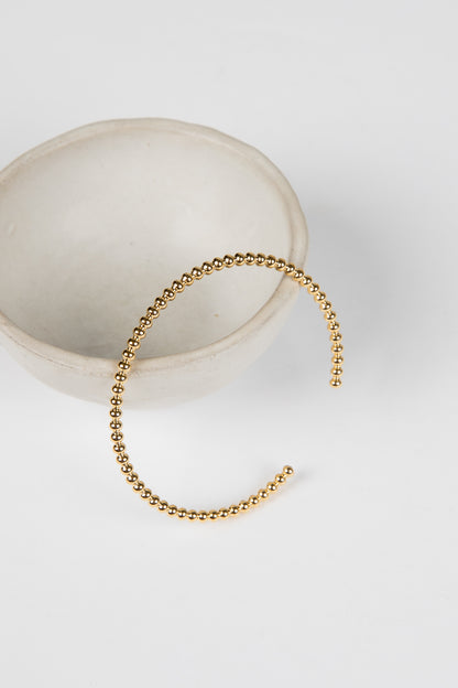 Gold beaded bracelet on a white surface with a neutral background
