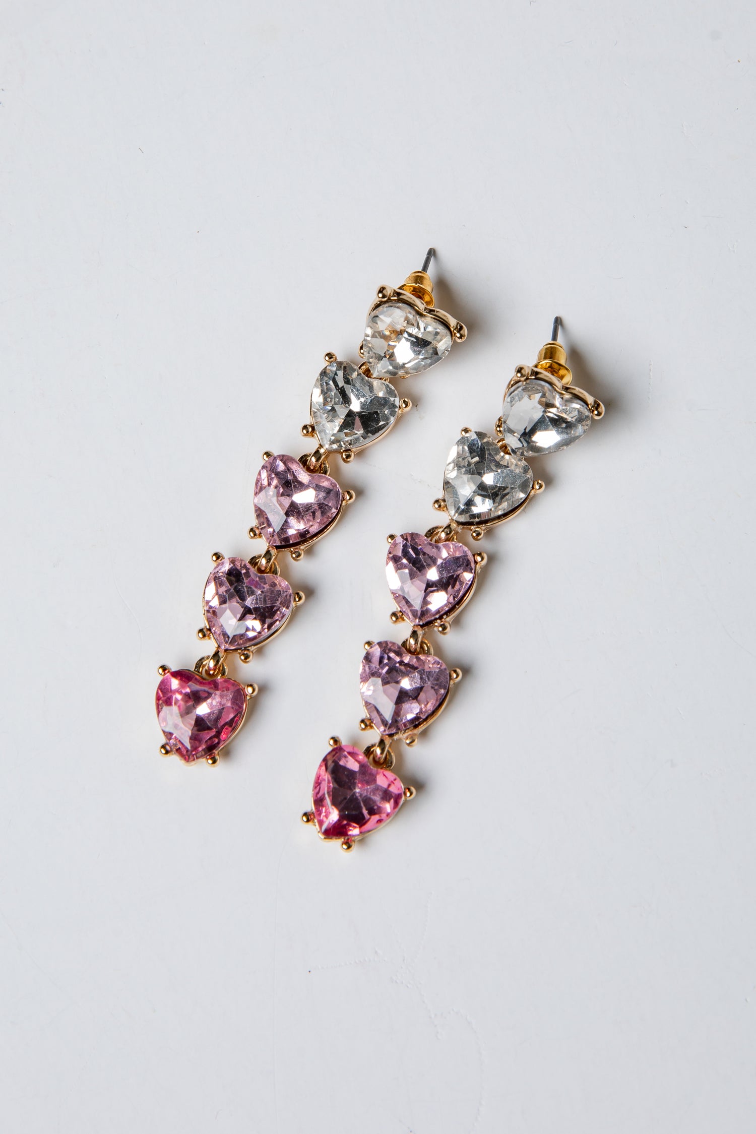 Pair of earrings with pink and clear gemstones on a light gray background