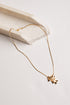 A delicate gold chain necklace with a small cluster of geometric bar pendants, styled on a light beige stone prop against a clean white background.