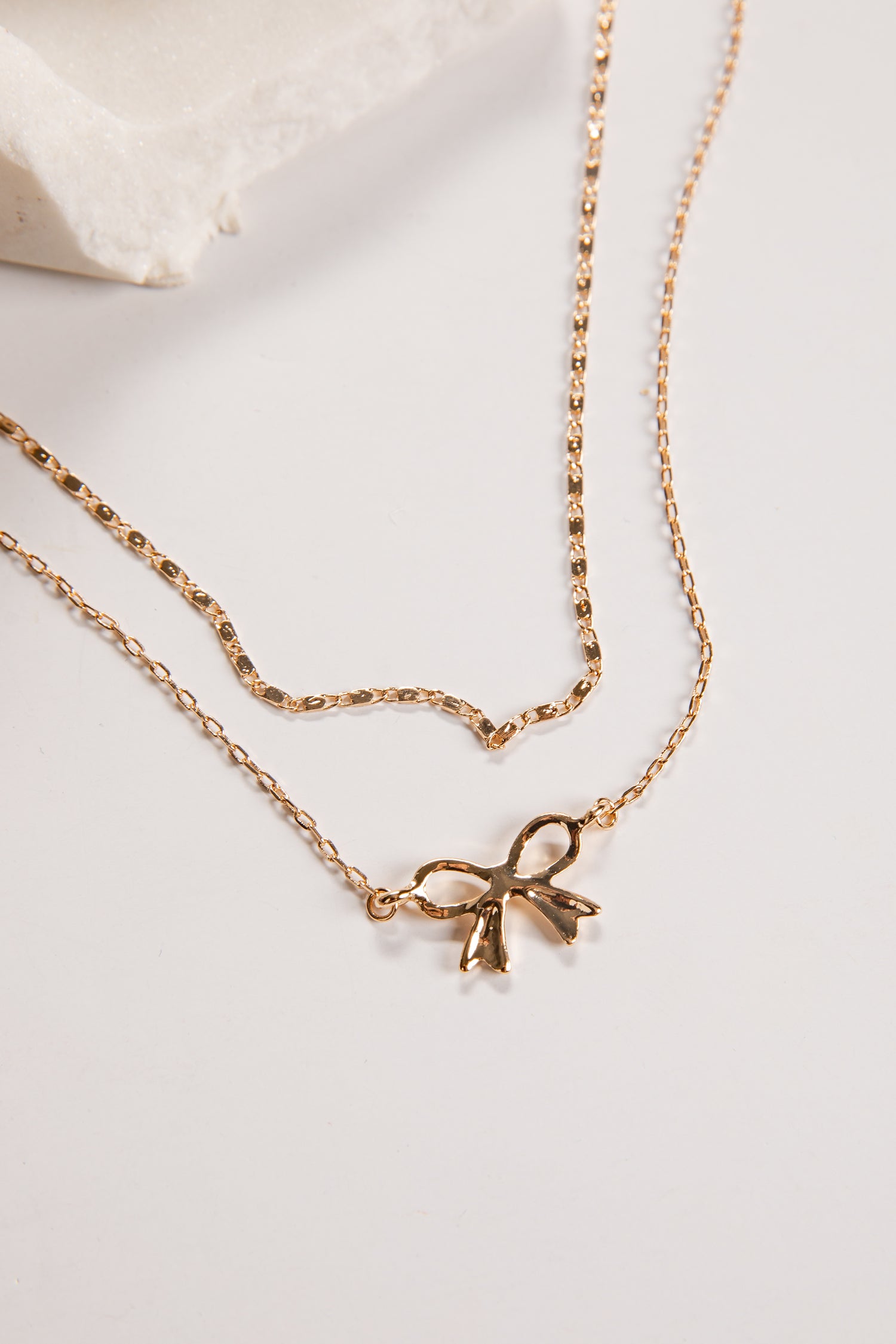 Gold necklace with a bow pendant on a light background