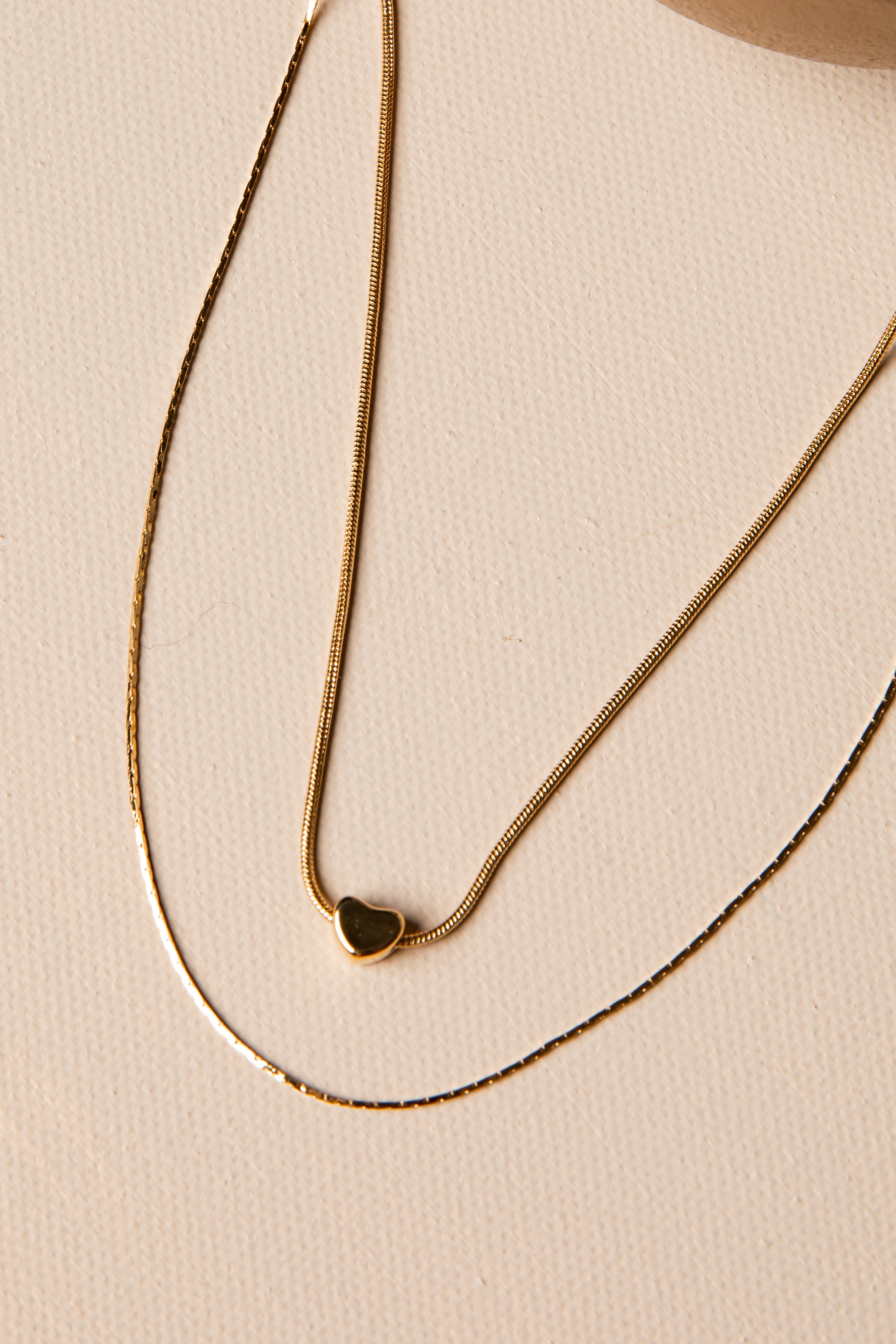 Gold necklace with a heart pendant on a beige background