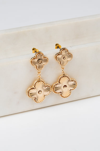 Gold floral earrings on a white marble surface