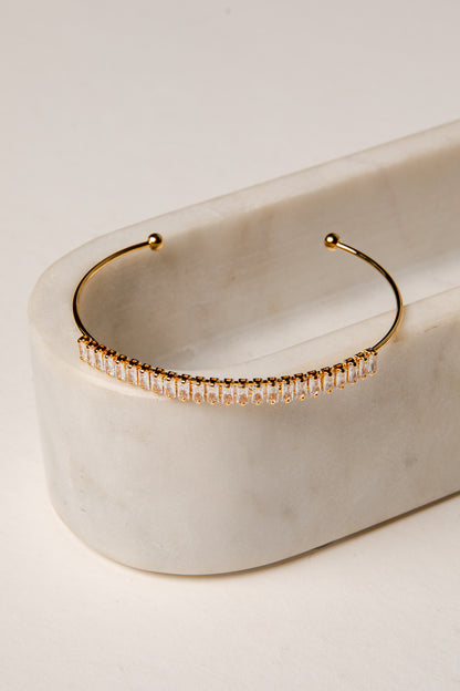 Gold hoop earring with embedded stones on a marble surface