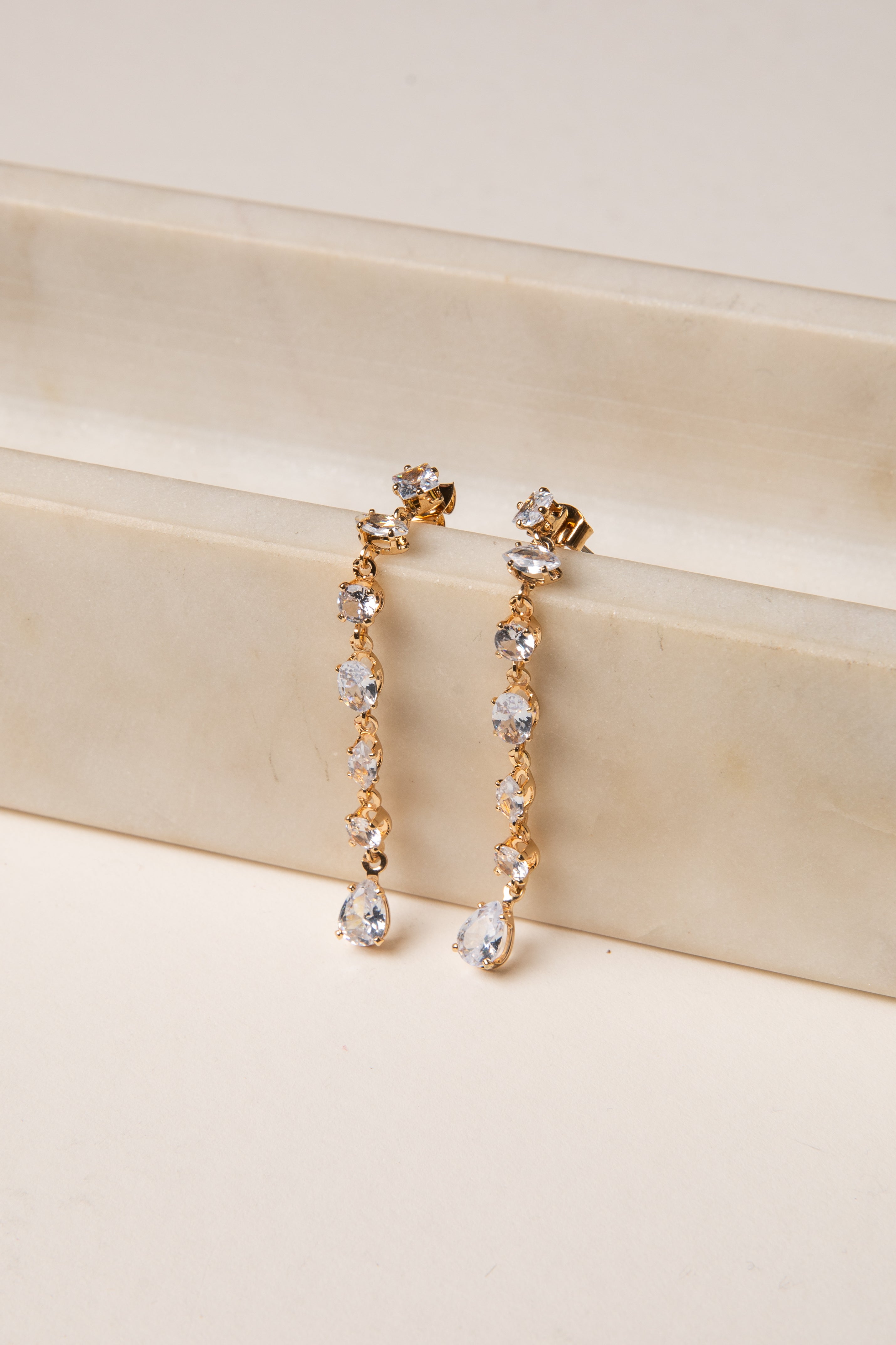 Gold and crystal drop earrings on a beige surface