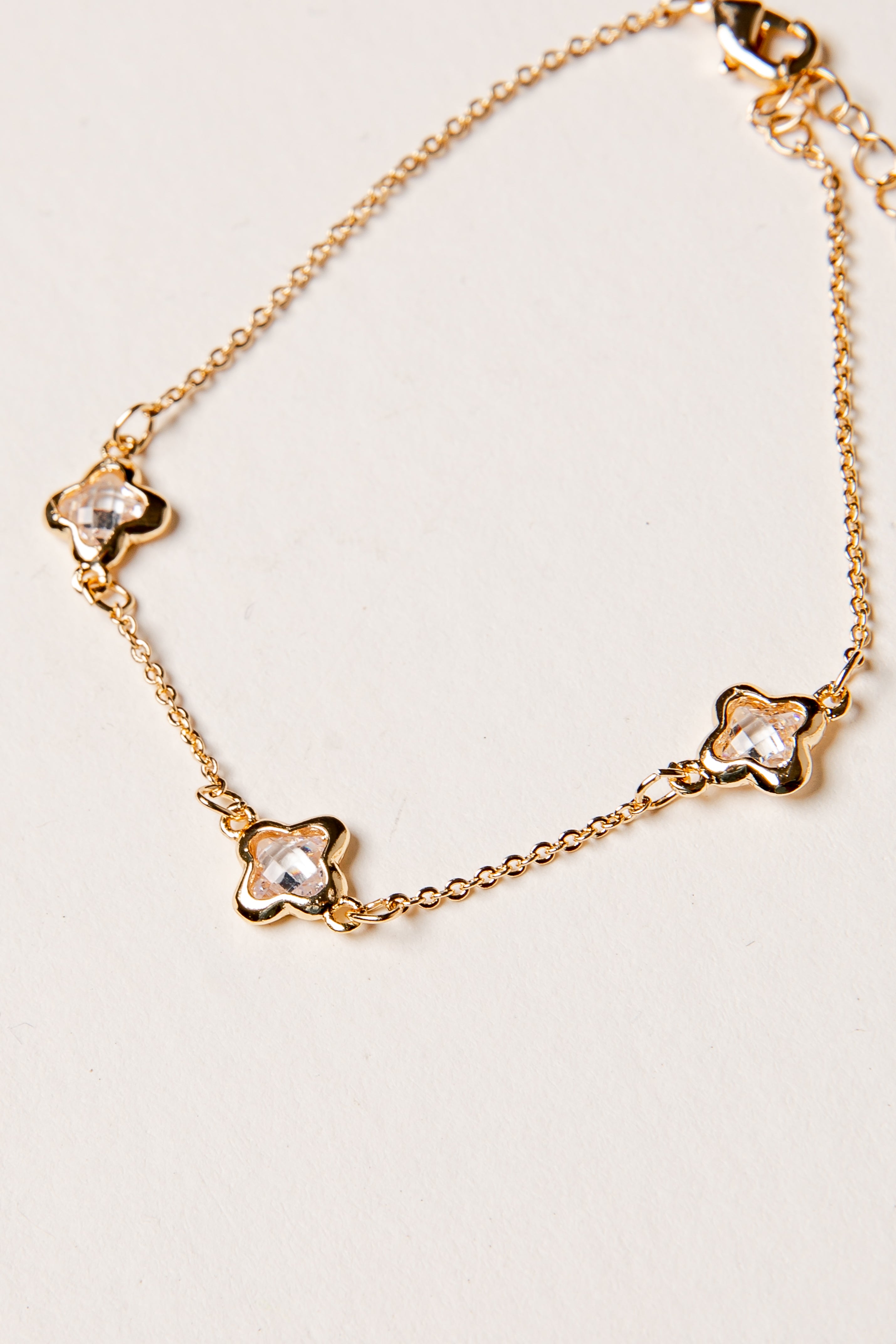 Gold bracelet with clover-shaped charms on a light background