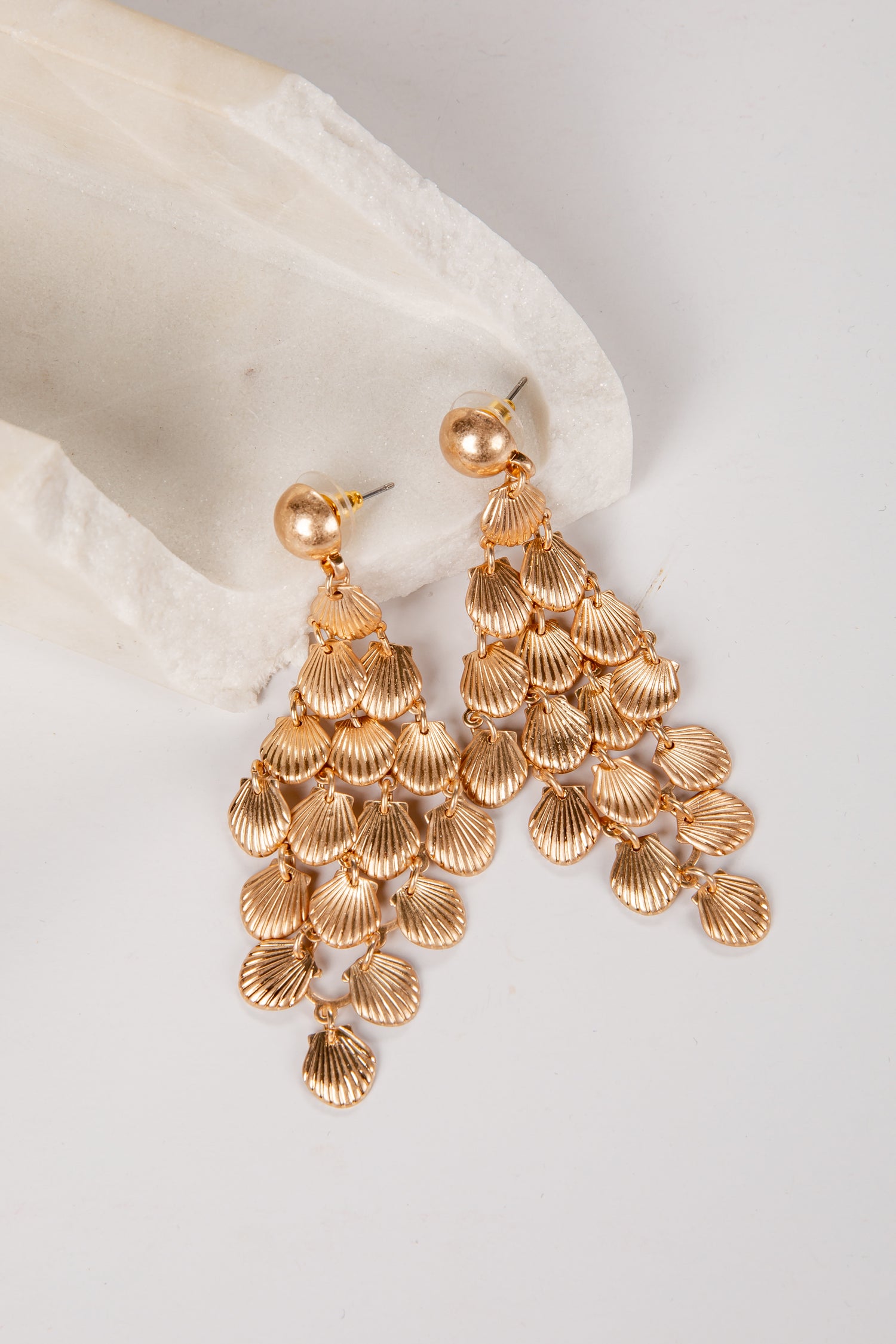 Gold chandelier earrings on a white fabric background