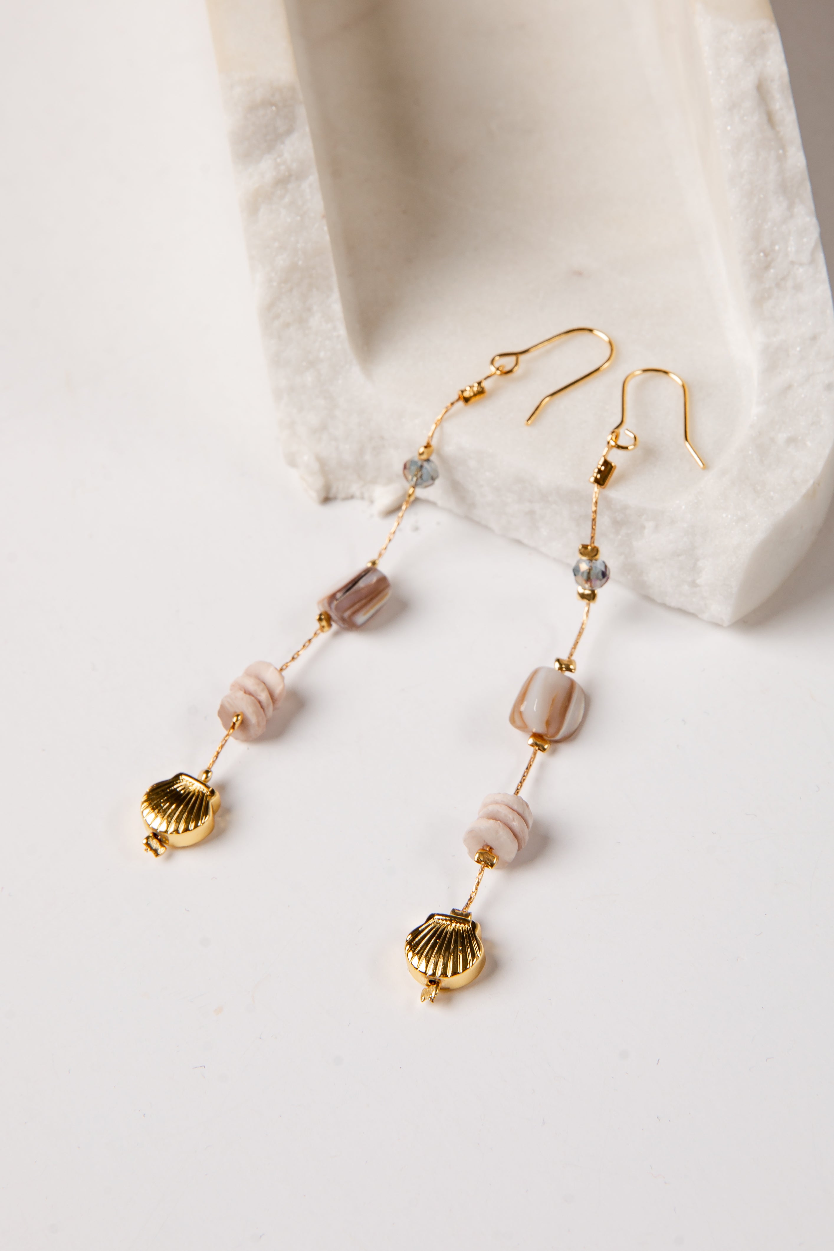 Gold earrings with shell and bead details on a white surface