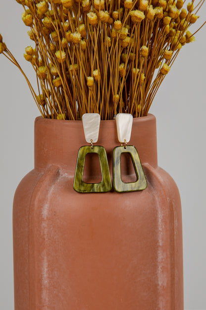 Terracotta vase with dried flowers and a pair of green earrings on a gray background