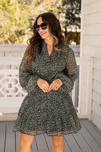 Woman wearing a black floral dress on a wooden deck with trees in the background