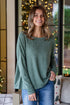 Woman wearing a green sweater and blue jeans standing in a room with decorative lights.