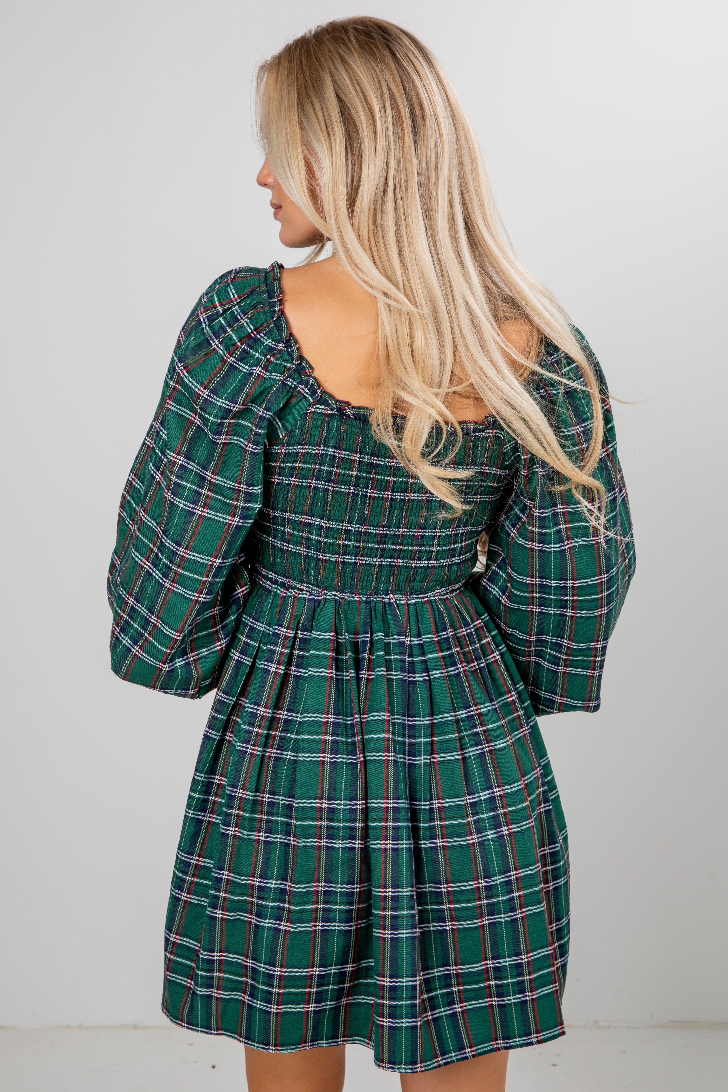 Woman wearing a green plaid dress with long sleeves against a white background